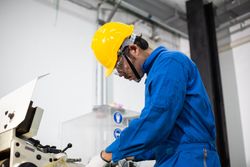 Male in blue jumpsuit and PPE gear operating machinery in plant