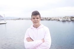 Young male teenager with crossing arms standing on the coast while looking at camera