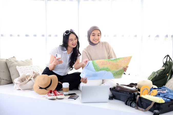 Two Young Asian Women Preparing Travel Suitcases, Looking at Maps for Travel Plans