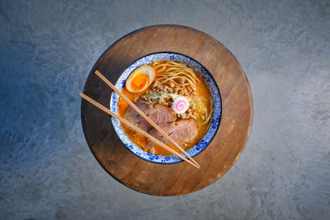 Chopsticks on bowl of Asian noodle soup served on wooden tray