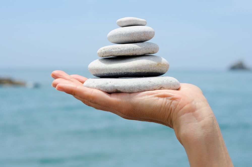 Side view of hand with small pile of rocks with ocean in background