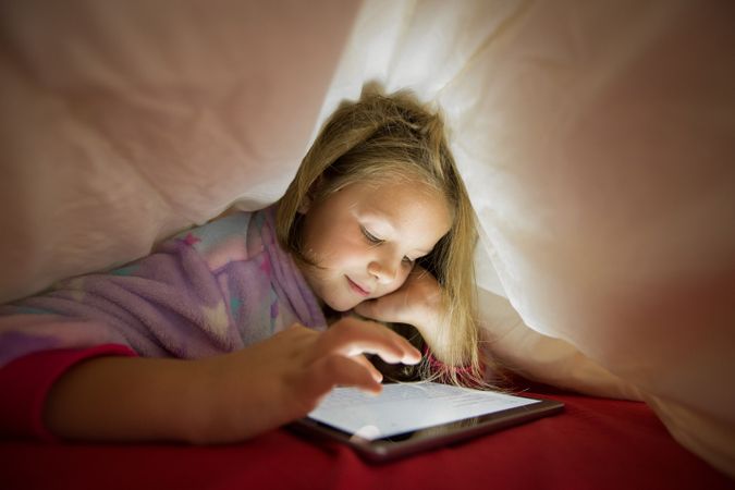 Girl using tablet under blanket