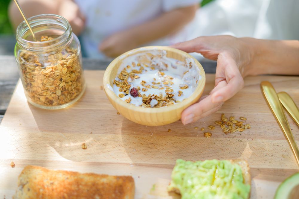 Unrecognizable mother and kid preparing yogurt with granola in park