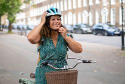 Happy Black woman adjusting helmet while sitting on bike 0gvQ3b
