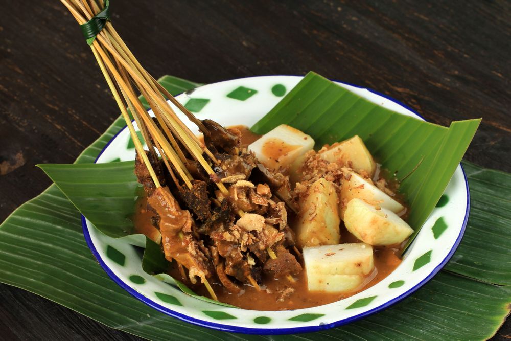 Bowl of beef sate skewers in spicy peanut sauce served on banana leaf