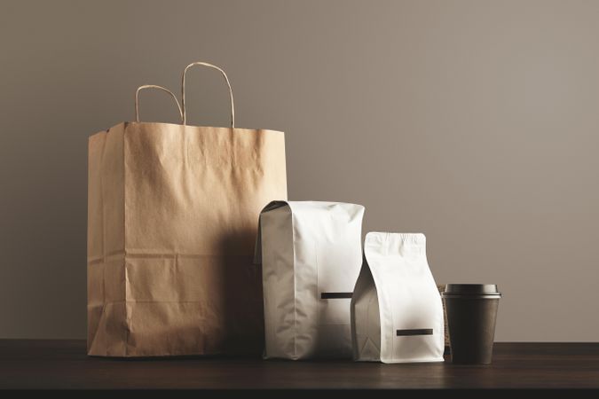 Two bags of coffee beans with brown paper bag and to-go cup