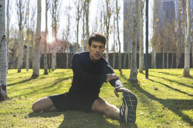Sporty man stretching legs after jogging in city public park