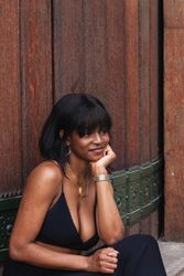 Cheerful Black woman in black outfit against wooden wall