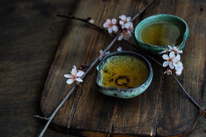 Green tea in cups and blooming peach tree branch on wooden table with copy space