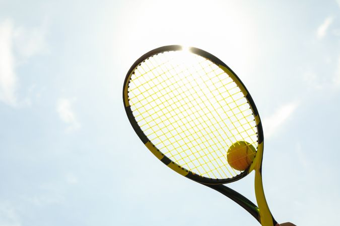 Tennis racquet with tennis ball against sky background