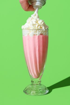 Strawberry milkshake topped with whipped cream, minimalist on a green background