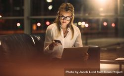 Young businesswoman texting on mobile phone while working on laptop late in office 5nPXmb