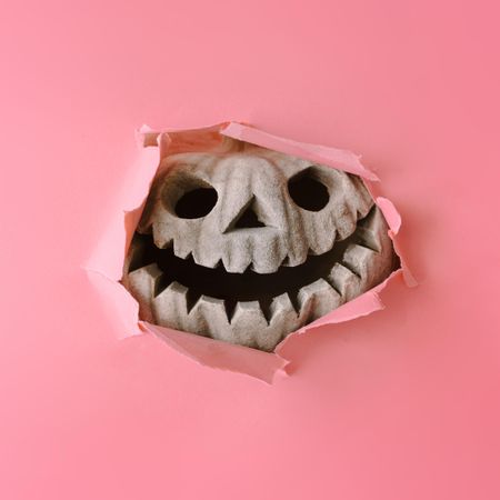 Pumpkin skull breaking through pastel pink wall
