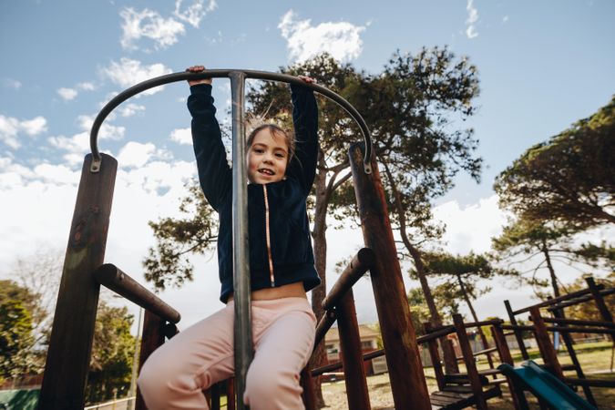 Portrait of young girl hanging on a climbing frame by her arms