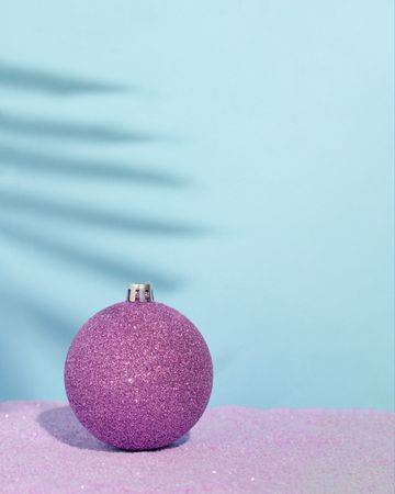 Christmas bauble on a beach with violet sand and palm tree shadow