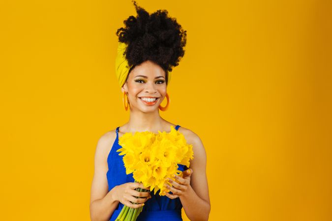 Portrait of smiling Black woman with large earrings holding a bouquet of daffodils