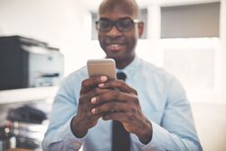 Man dressed in shirt and tie texting in home office