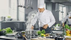 Famous Chef of a Big Restaurant Prepares Dishes with His Help of Cooks. Modern Kitchen is Made of Stainless Steel and Full of Cooking Ingredients.