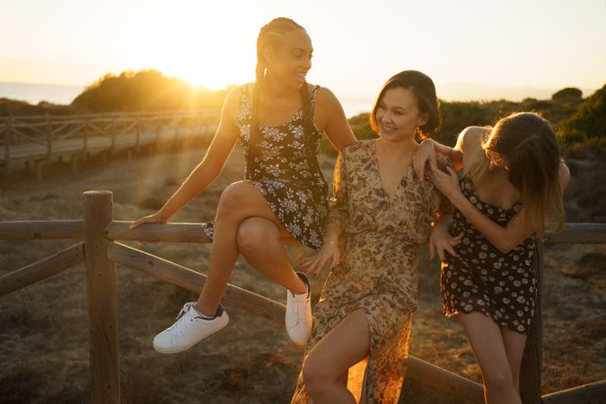 Happy women in summer dresses sitting on wooden fence at magic hour