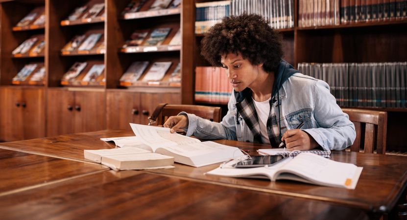 Focused college student studying in library with textbooks on desk