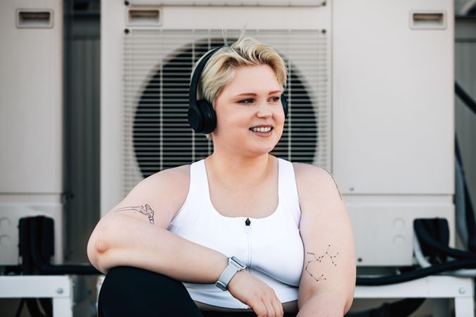 Happy woman with tattoos, smart watch and headphones in front of fans on rooftop