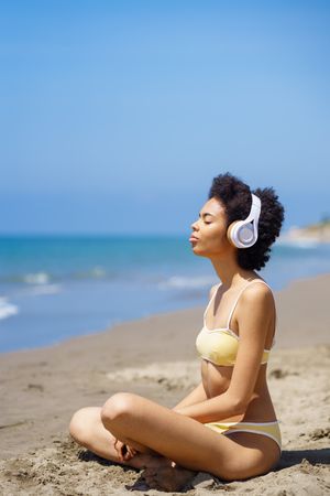 Woman in yellow swimwear sitting and meditating on beach looking out to the ocean, vertical