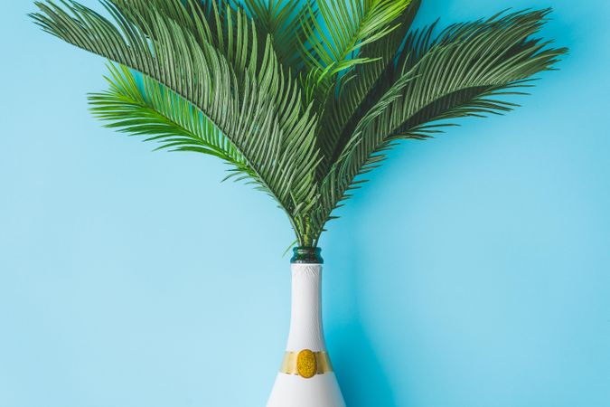 Champagne bottle with tropical green palm leaves on pastel blue background