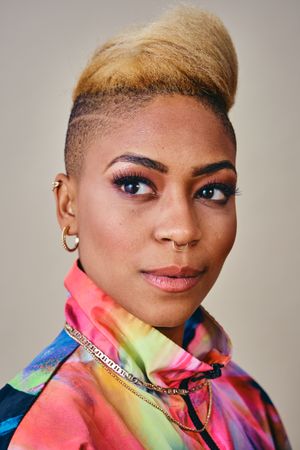 Close up studio shot of Black woman in bold 80s windbreaker jacket and gold jewelry