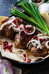 Close up of Georgian dish of abkhazura meat cutlets on plate with pomegranate seeds and onions