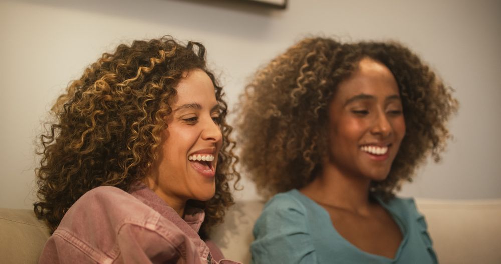 Portrait of Two Brazilian Young Women Using Laptop Computer While Sitting on a Sofa at Home.