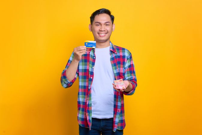 Happy calm Asian man holding credit card and cash in studio shoot