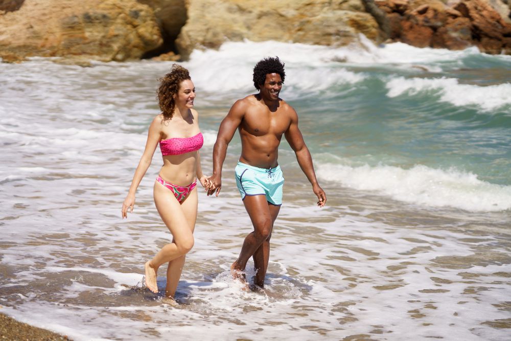 Happy diverse man and woman walking on wet coast
