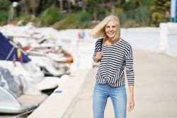 Smiling older woman in jeans and striped shirt standing outside on sunny day