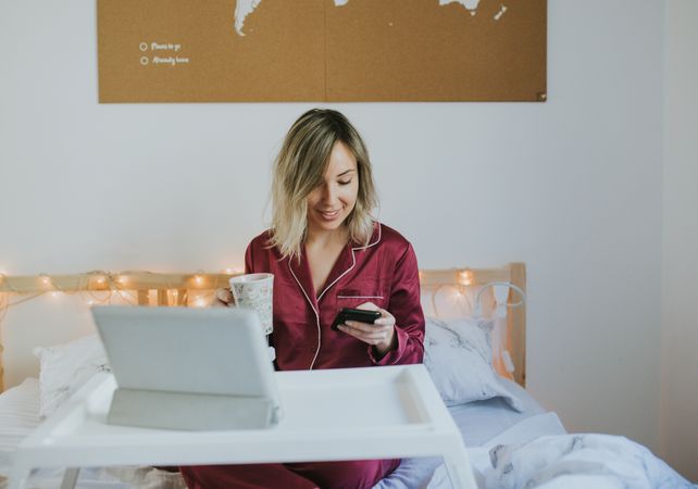 Woman sitting in bed with tablet and looking on smartphone