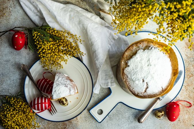 Top view of Easter food concept with traditional cake dusted with sugar and colorful eggs decorated with yellow spring flowers