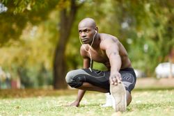 Fit male stretching lower body with shirt off listening to music on headphones