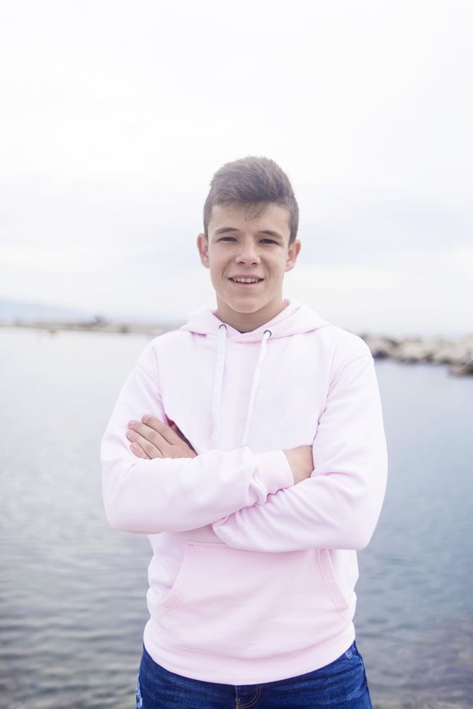 Young male teenager with crossing arms standing on promenade while looking at camera, vertical