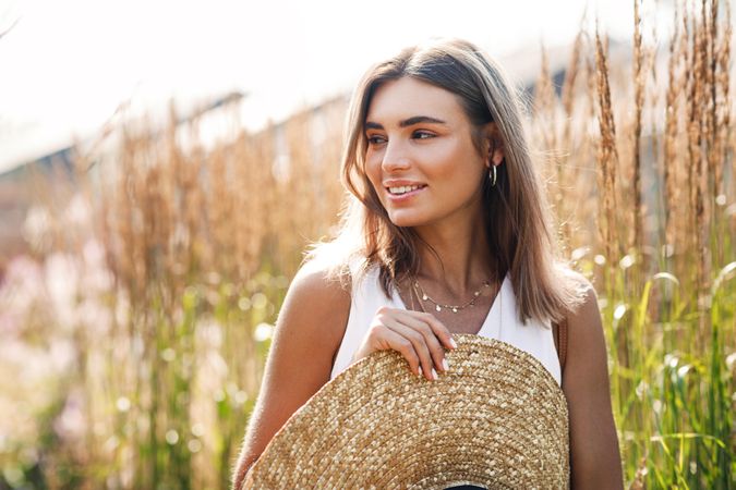 Woman in beige top holding a straw hat on sunny day