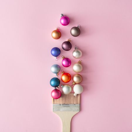 Paint brush with Christmas ornaments on pastel pink table