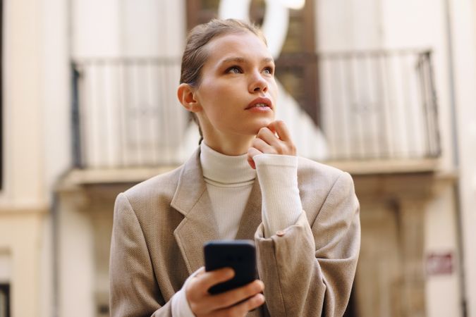 A Young Woman Deep in Thought as She Engages with Her Smartphone in a Bustling Urban Setting