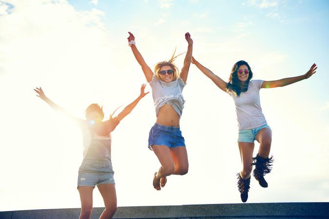 Happy female friends jumping for joy on sunny day