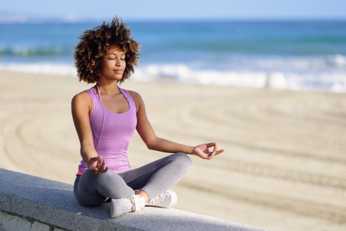 Black woman with afro hairstyle meditating on the coast