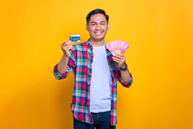 Happy Asian man holding credit card and cash in studio shoot