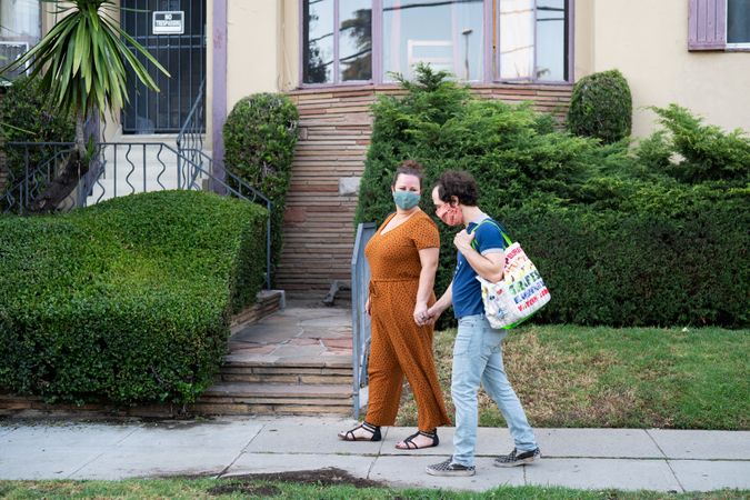Side view of married couple walking down the street with grocery bags wearing masks