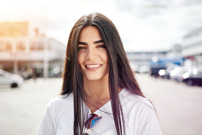 Woman with long brown hair smiling at camera on sunny day