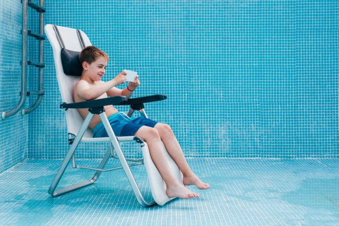 Boy with smartphone sitting on bottom of empty pool