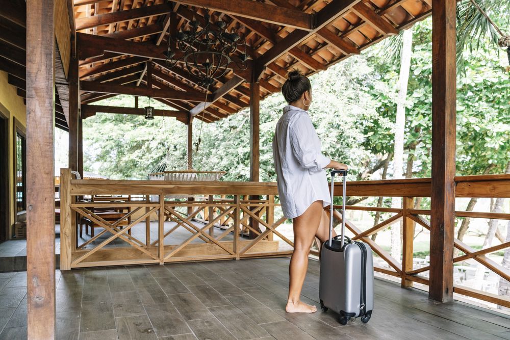 Joyful woman in bikini carrying suitcase at hotel terrace