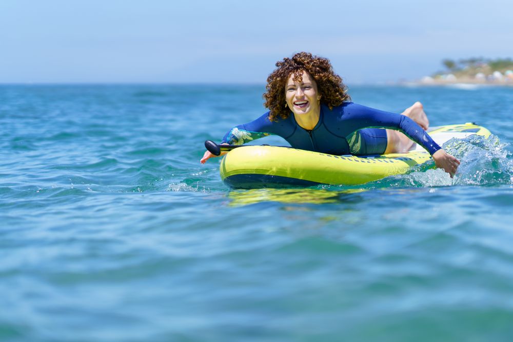 Cheerful woman pulling SUP board in seawater