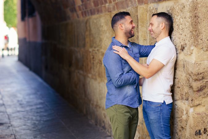 Two men facing each other lovingly under a city bridge