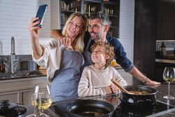 Cheerful diverse family taking selfie on mobile phone in kitchen